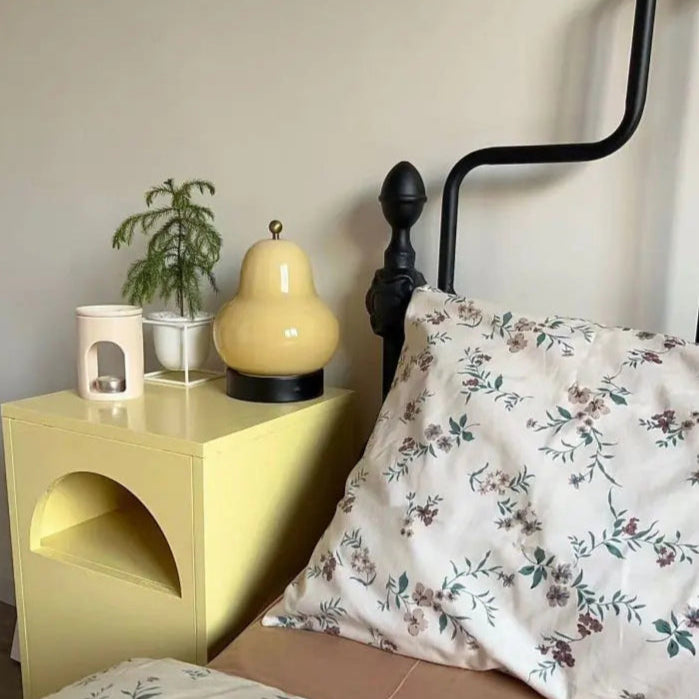 Yellow nightstand with a pear-shaped lamp next to a bed with floral bedding.
