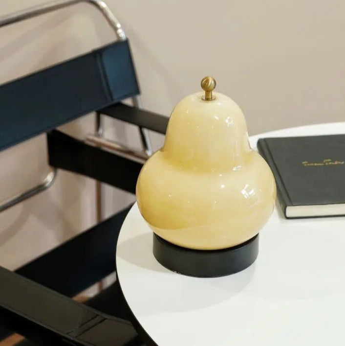 Decorative pear-shaped lamp on a round table with a chair and notebook in the background.